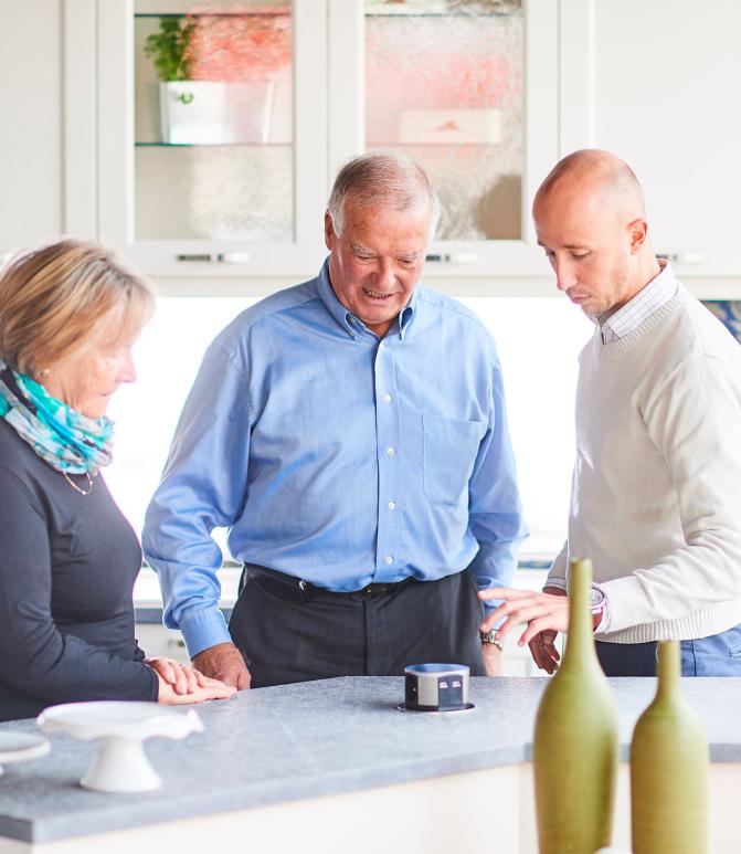 Trois personnes discutent autour d’un îlot de cuisine moderne, en testant une prise escamotable intégrée au plan de travail.
